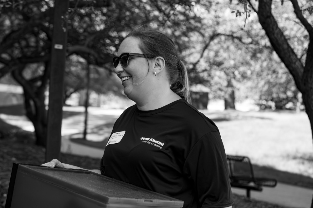 Black and white picture of GVSU Alumna smiling as she carries a box